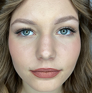 A woman with long brown hair and blue eyes, featuring long eyelashes that enhance her striking gaze.