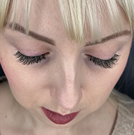 A woman with blonde hair and long eyelashes gazes thoughtfully, her features highlighted by soft lighting.