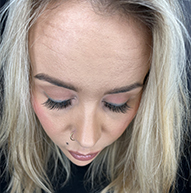 A woman with blonde hair and a piercing, emphasizing her long eyelashes and bold style.