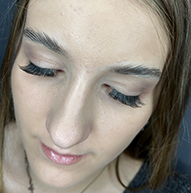 Close-up of a woman with long eyelashes, head slightly tilted down, eyes closed, highlighting her thick lashes.