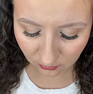 A woman with long curly hair dressed in a white shirt, accentuating her striking lashes and graceful appearance.